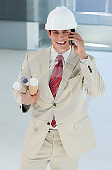 Smiling male architect with hardhat on phone