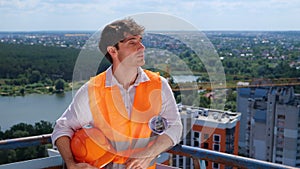 Smiling male builder looking on the construction site while holding helmet and drawing. Business, building, industry