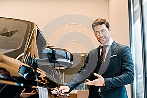 smiling male car dealer in eyeglasses pointing at black automobile