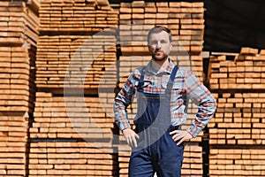 Smiling male carpenter doing an inventory in a warehouse. standing next to a pile of wood bars in a workshop