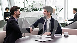 Smiling male colleagues shake hands getting acquainted at meeting