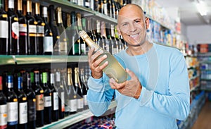 Smiling male consumer choosing bottle of wine in store