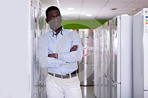 Smiling male customer standing near fridges in store of appliances