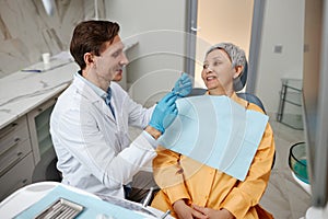 Smiling male dentist working with senior woman at office in dental clinic.