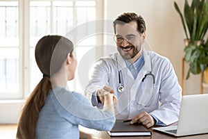 Smiling male doctor handshake female patient at consultation