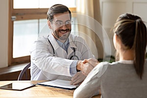 Smiling male doctor handshake female patient at consultation