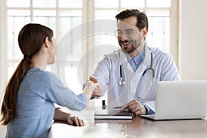 Smiling male doctor handshake female patient in hospital