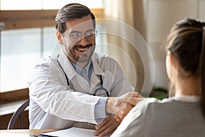 Smiling male doctor handshake female patient at meeting