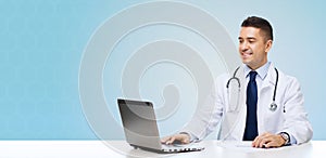 Smiling male doctor with laptop sitting at table