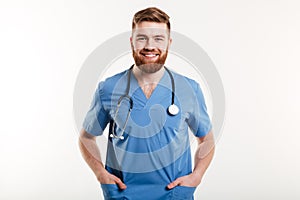 Smiling male doctor standing with stethoscope and holding hands in pockets