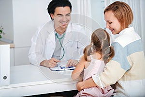 Smiling male doctor talking to, cheering up his little patient.