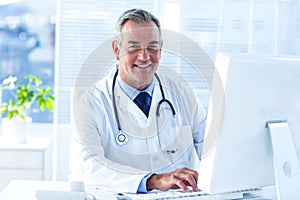 Smiling male doctor using computer in clinic