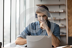 Smiling male in earphones study online on laptop