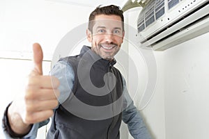 smiling male electrician gesturing thumbs up near air conditioner