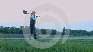 Smiling male farmer with shovel walking along the field. Worker wearing straw hat. Agriculture business concept. Real