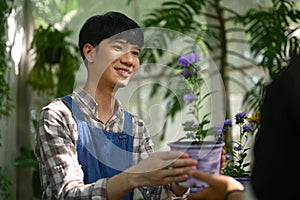 Smiling male florist giving plant in a pot to female customer at his floral shop. Floristry and small business concept.