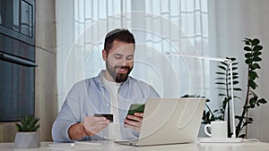 Smiling male freelancer using smartphone and credit card for paying online bills