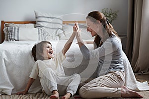 Smiling male kid rejoicing hitting palm clapping hands to woman nanny playing together