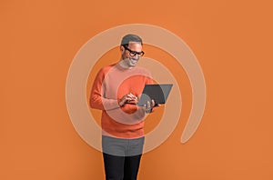 Smiling male manager checking e-mails over laptop while standing confidently on orange background