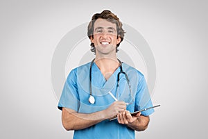 Smiling male nurse in scrubs writing on clipboard