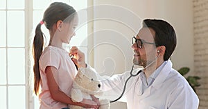 Smiling male paediatrician holding stethoscope examining cute little child girl