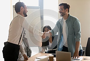 Smiling male partners greeting handshaking at diverse corporate group meeting