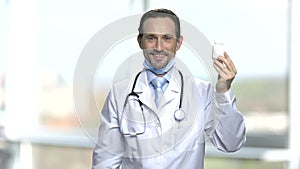 Smiling male physician showing bottle of pills.