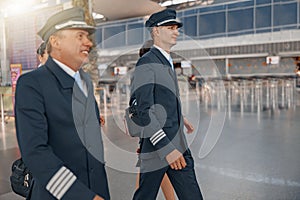 Smiling male pilots walking along the airport terminal