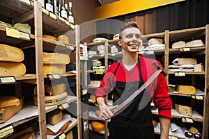 Smiling male salesperson holding knife in cheese store