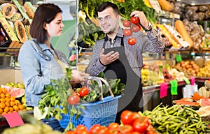 smiling male shopping assistant helping customer to buy fruit and vegetables in grocery shop