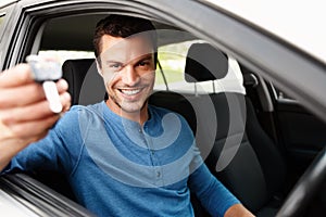 Proud new car owner. Smiling male sitting in his car holding up his car keys.