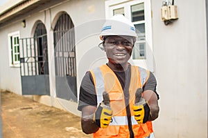 Smiling male standing outdoors with his thumbs up in the air and wearing a construction hard hat