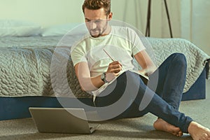 Smiling male student working on home assignment at laptop