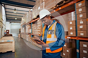 Smiling male supervisor checking stock records in digital tablet standing near the stack of boxes