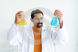 Smiling Male teacher in white lab coat with safety glasses with laboratory tools background in elementary school