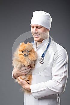 Smiling male vet with phonendoscope holding cute pomeranian dog