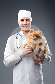 Smiling male vet with phonendoscope holding cute pomeranian dog