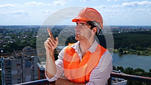 Smiling male worker in helmet counting and pointing with a finger at the construction site on the roof. Business