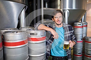 smiling male worker holding beer glass while standing at factory