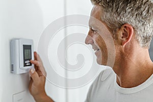 Smiling Man Adjusting Thermostat On Home Heating System