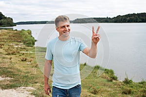 A smiling man with an athletic body, dressed in denim shorts and a blue T-shirt, walking on the banks