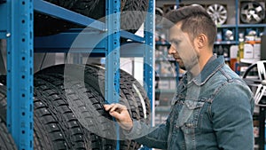 Smiling man auto mechanic carrying new tire in tire store choosing for his car