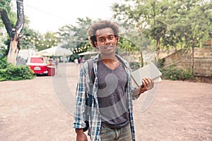 Smiling man with backpack standing and holding books outdoors