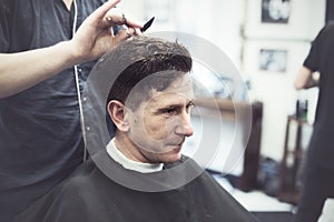 Smiling man in barbershop watching the process of hair cutting