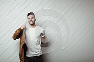 Smiling man in blank t-shirt and jacket, white wooden wall background