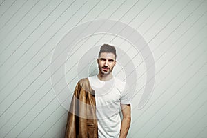 Smiling man in blank t-shirt wearing leather jacket on the shoulder, white wooden background