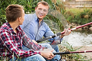 Smiling man and boy fishing together on river