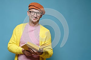 Smiling man in bright clothes, holding an open book in hands and looking at the camera. Funny creative person. Copy