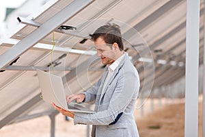 A smiling man checks the work of solar panels through a laptop. Outdoors