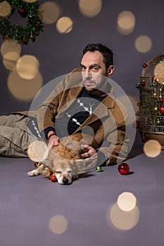 Smiling man in a christmas location on a gray background with a dog in his arms